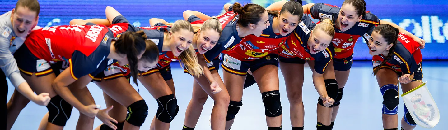 A team of athletes in red and blue uniforms huddle together on a court, cheering with excitement.